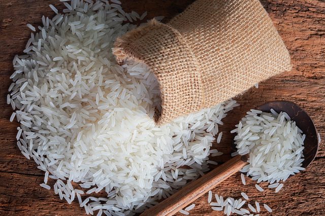 White uncooked Thailand jasmine rice in small burlap bag with wooden spoon on wood table.