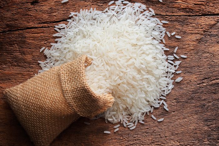 White uncooked Thailand jasmine rice in small burlap bag on wood table.