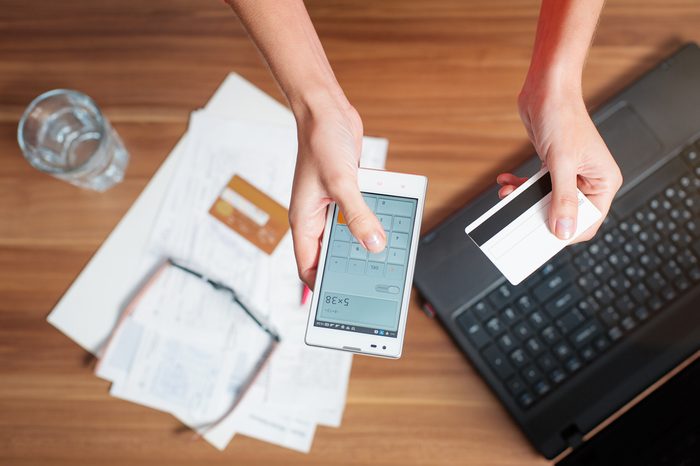 Business work place with female hands holding smart phone and bank card, top view