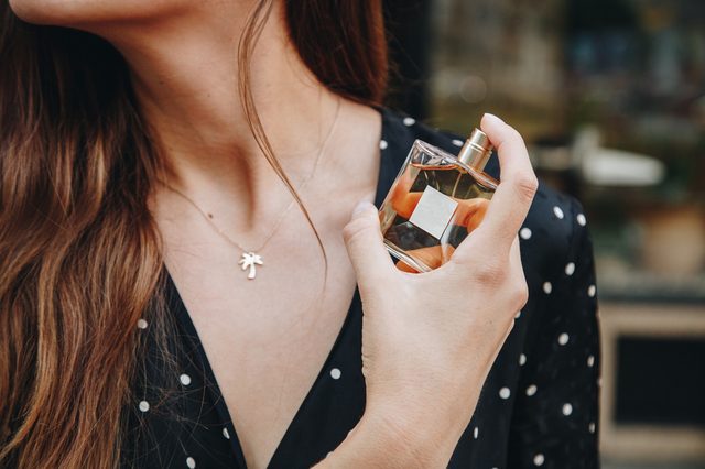 young woman wearing black and white polka dot dress posing with a bottle of expensive perfume. beautiful and stylish european fashion blogger posing with perfume outdoors. perfect summer outfit. 