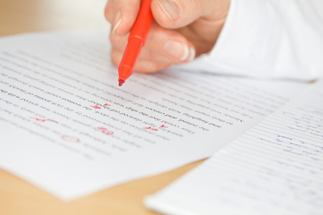 Proofreader with red pen checks a transcription of some hand written text