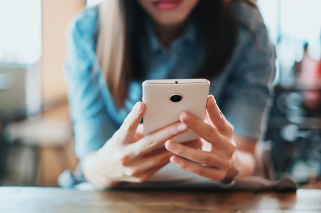 Hand of woman using smartphone on wooden table,Space for text or design.