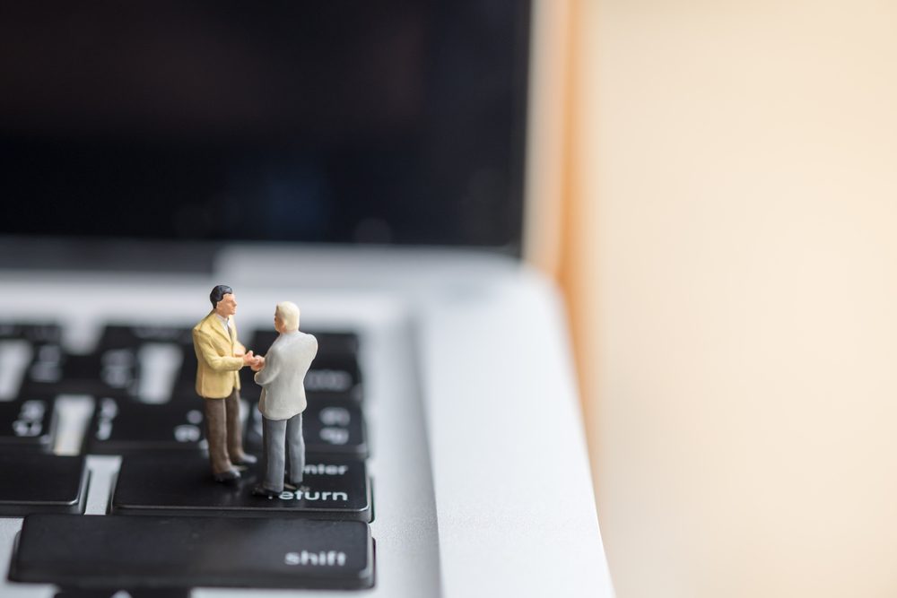 Business and computer Concept. Two businessman miniature figures handshake on laptop computer.