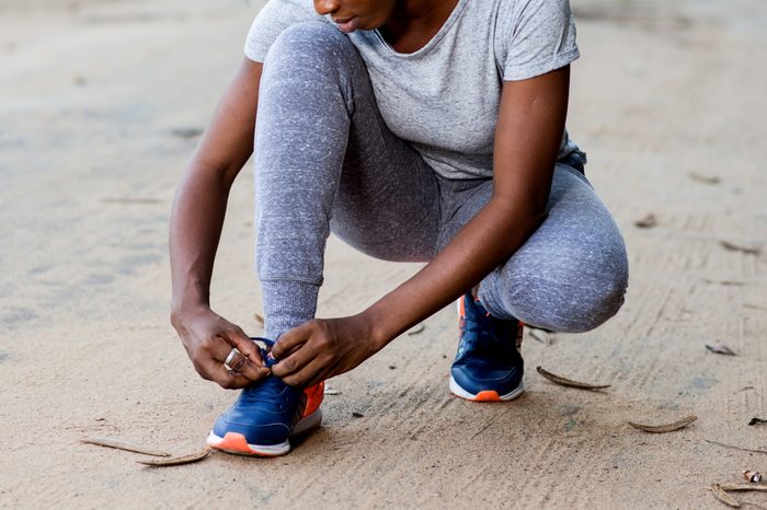 young girl in sportswear squatting on a track and ties her laces for sport.