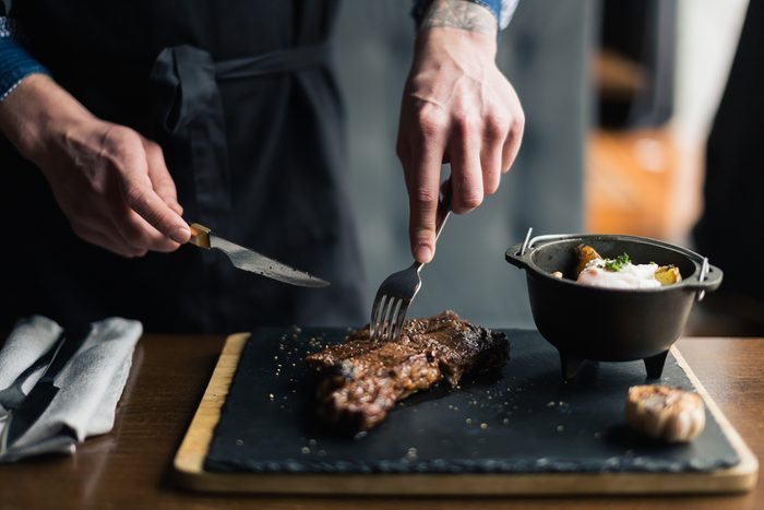 man slicing cooked medium rib eye steak on board, wide photo