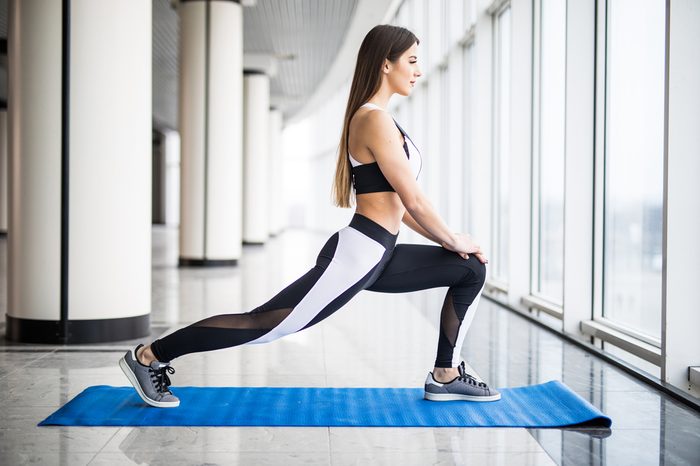 Stretching after great workout. Young beautiful young woman in sportswear doing stretching while standing in front of window at gym