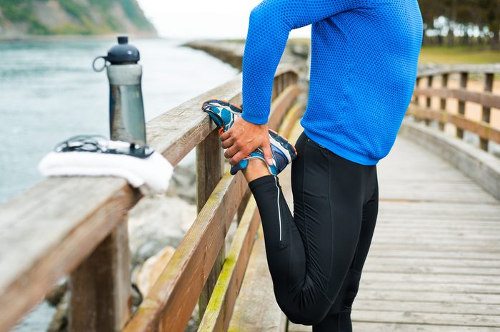 Fit sports man doing stretches before an outdoor running training on a cloudy autumn day with a sport bag on a wooden walkway. Fitness sporty man in Rodiles, Asturias.