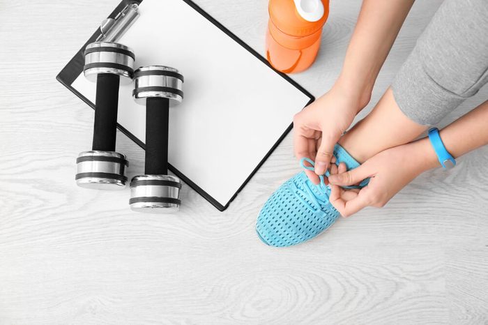 Young woman tying shoelaces on floor, flat lay. Ready for gym workout