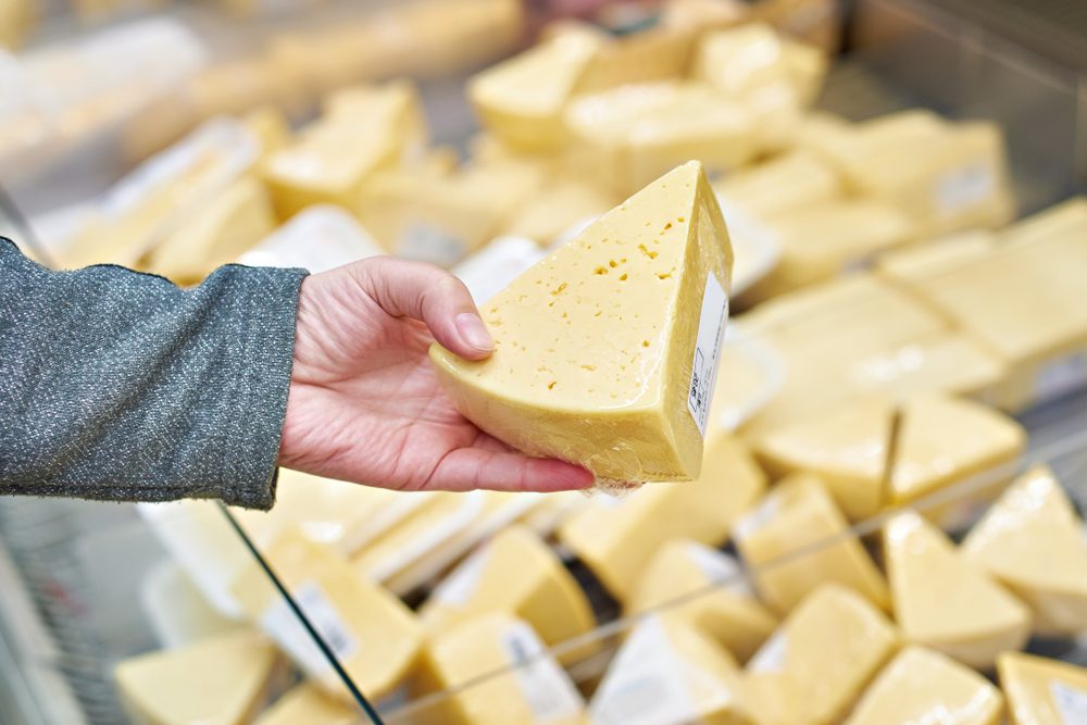 Hand of the buyer with a piece of cheese in the store