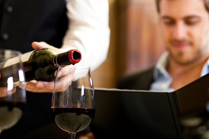 Waiter pouring red wine to a man