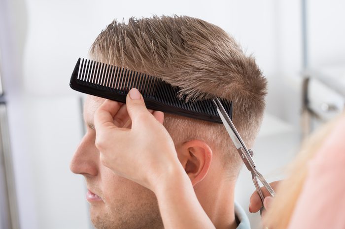 Young man getting haircut from female hairdresser at salon