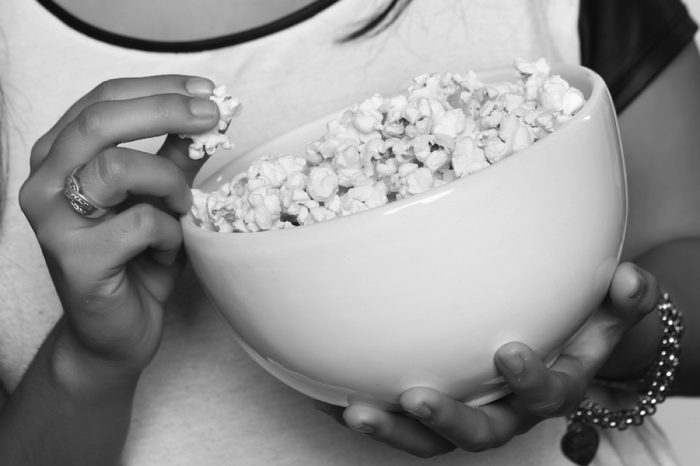 Young beautiful woman eating popcorn. Isolated white background