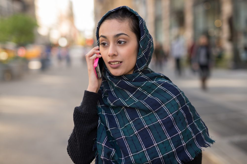 Young woman wearing hijab head scarf in city talking on cell phone