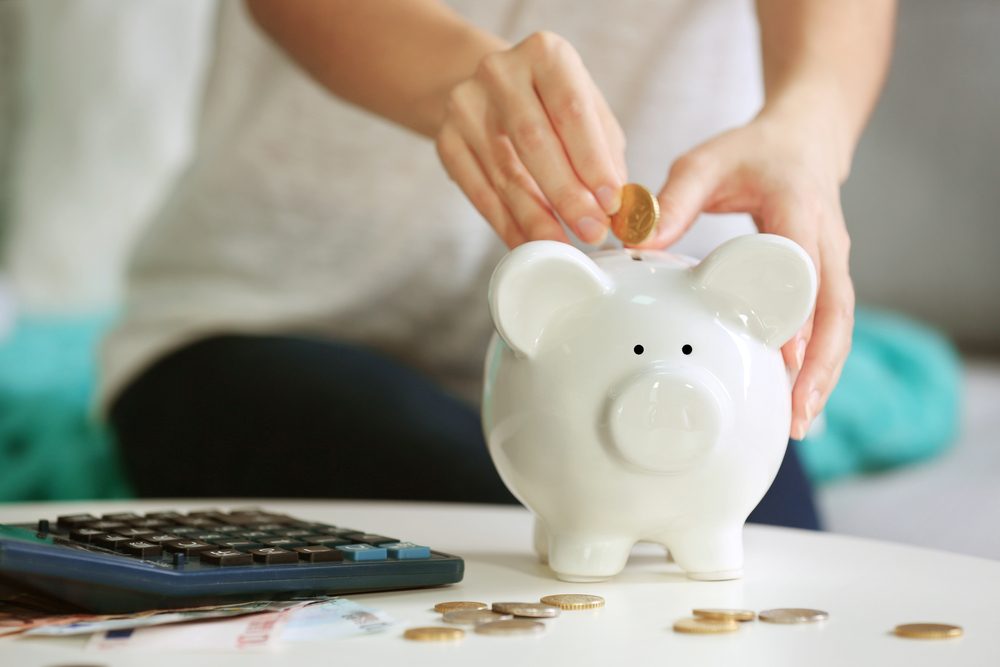 Female hand putting coin into piggy bank closeup