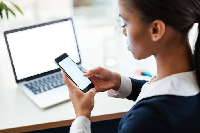 Top view of Afro Business woman in dress sitting by the table with laptop and using phone in office. Cropped image. Side view