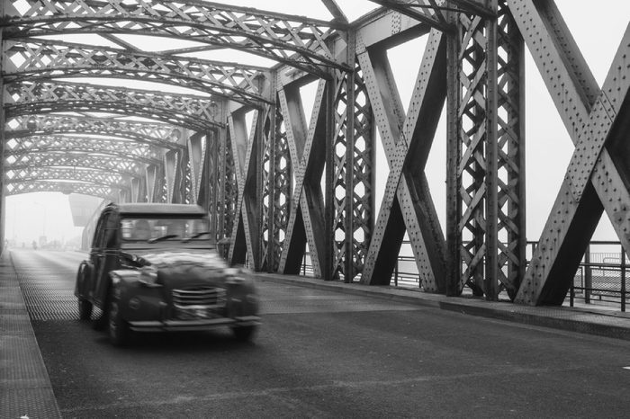 Old blue vintage car driving on the asphalt road of the city bridge on a foggy day in Dieppe, France. Old bridge tunnel metal structure. Urban scene, city life, transport and traffic concept. Toned