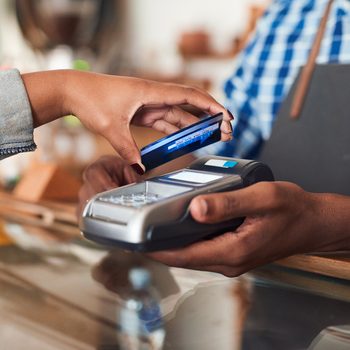 Closeup of a customer using her credit card and nfs technology to pay a barista for her purchase at a cafe