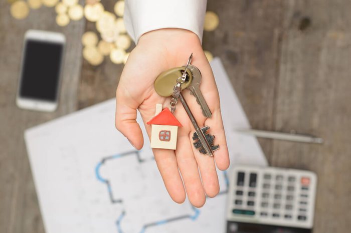 Real estate agent handing over a house key, desktop with tools, wood swatches and computer on background, top view