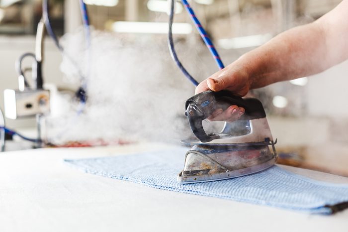 Professional ironing in dry cleaner detail of iron and hands. Presser in sewing clothes pressed