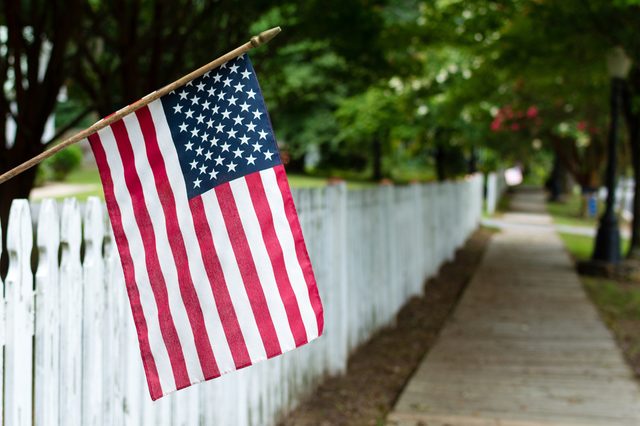 Small American flag hangs from a picket fence along the sidewalk in a rural town.