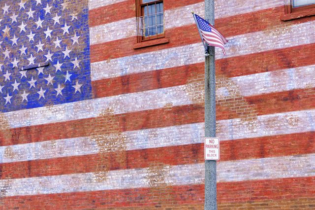 Small-town street scene in Illinois: American flag flapping in breeze by huge painted American flag fading from brick wall