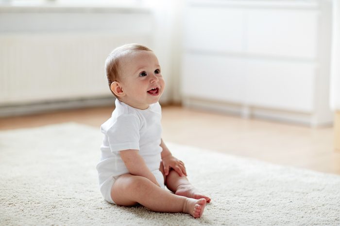 childhood, babyhood and people concept - happy little baby boy or girl sitting on floor at home