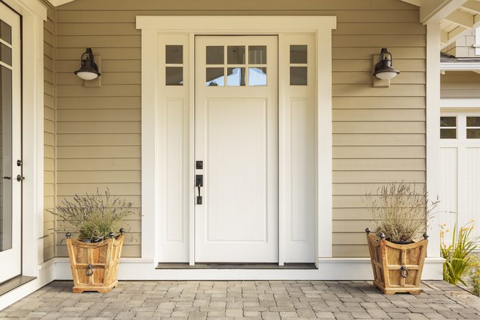 White front door with small square decorative windows and flower pots