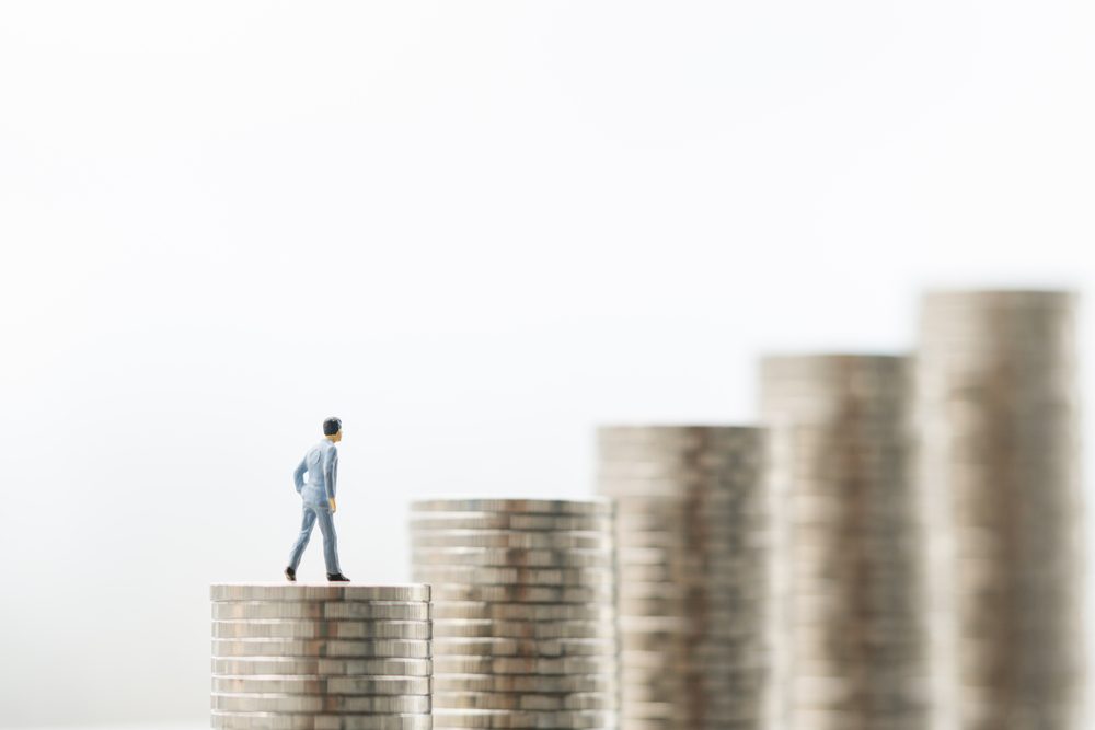 Miniature people: small figure businessman standing on a stack of coins with white background. Money, Financial, Business Growth concept.