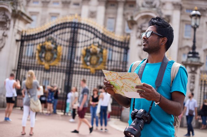 Indian tourist outside buckingham palace holding a map and his camera