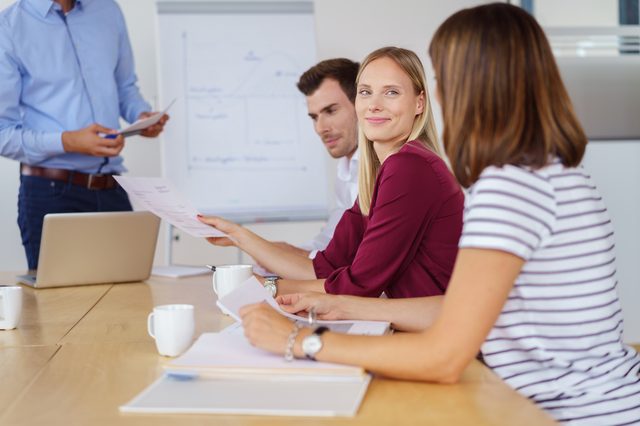 Young business team in a meeting seated around a table in the office with focus to a smiling businesswoman listening to a colleague