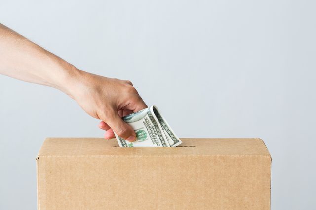 charity, finances, funding, investment and people concept - male hand putting dollar money into donation box