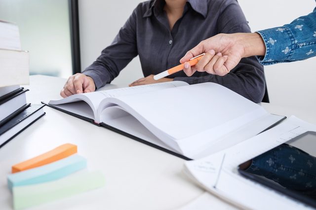 Education, teaching, learning, technology and people concept. Two high school students or classmates with helps friend catching up workbook learning in classroom, Tutor books with friends.