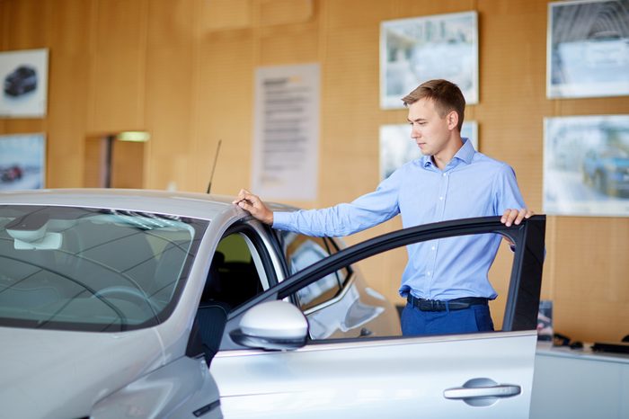 Beautiful young male is talking to handsome car dealership worker while choosing a car in dealership