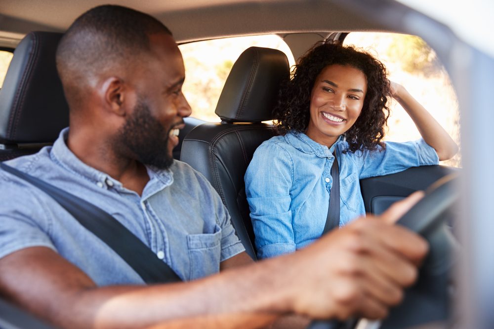 Young black couple in car on road trip smiling at each other