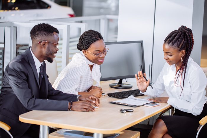 happy African couple and female seller sit at table and make a deal for sale of car