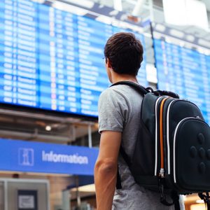 Young man with backpack in airport near flight timetable