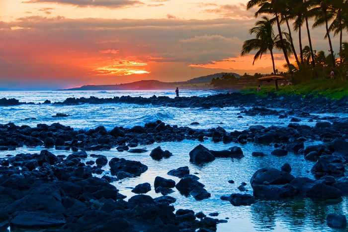 Palm trees silhouetted against a colorful tropical sunset and reflected in the Pacific Ocean on the island of Kauai, Hawaii, USA