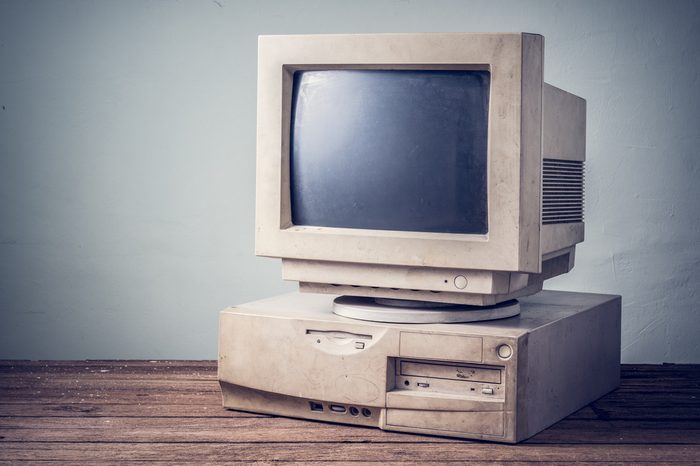 old and obsolete computer on old wood table with concrete wall background, vintage color tone