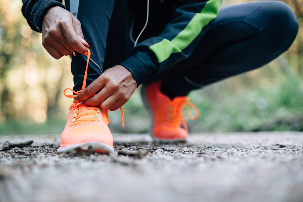 anonymous figure crouching to tie the laces of their sneakers on an outdoor path