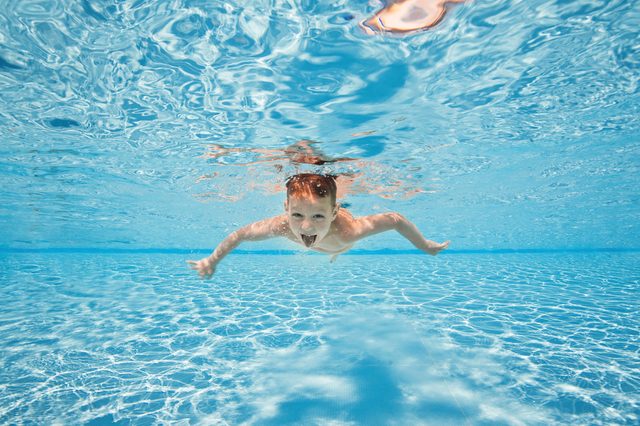 Happy young boy swim and dive underwater, kid breast stroke with fun in pool. Active healthy lifestyle, water sport activity and lessons with parents on summer family vacation with child.