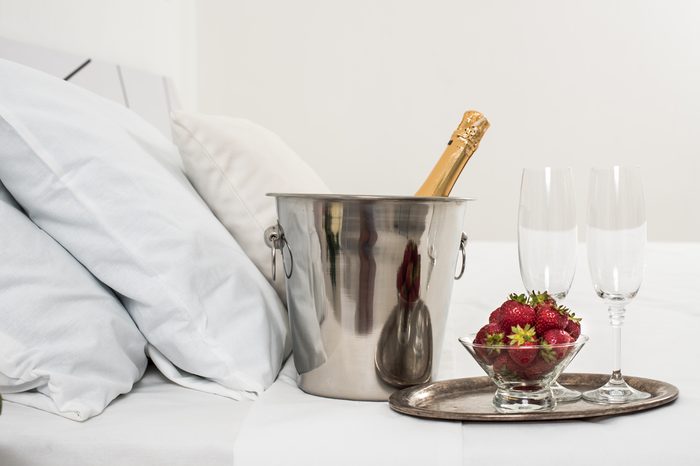 Champagne in bed in a hotel room, ice bucket, glasses and fruits on white linen