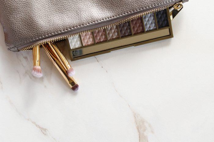 Silver make up bag emptying onto white marble counter with eyeshadow and gold make up brushes. White marble copy space.