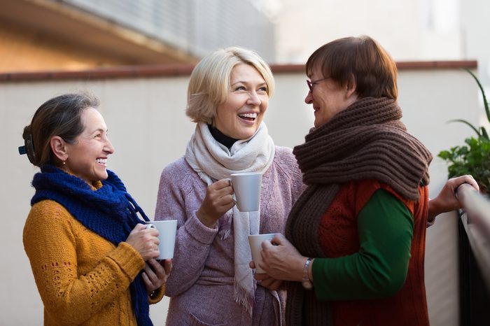 Portrait of cheerful senior female friends drinking coffee at patio. Focus on blonde