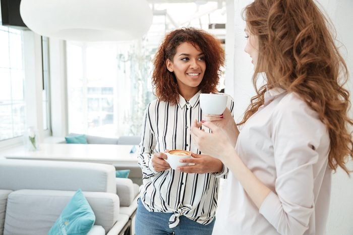 Young smiling friends talking in cafe while drinking coffee