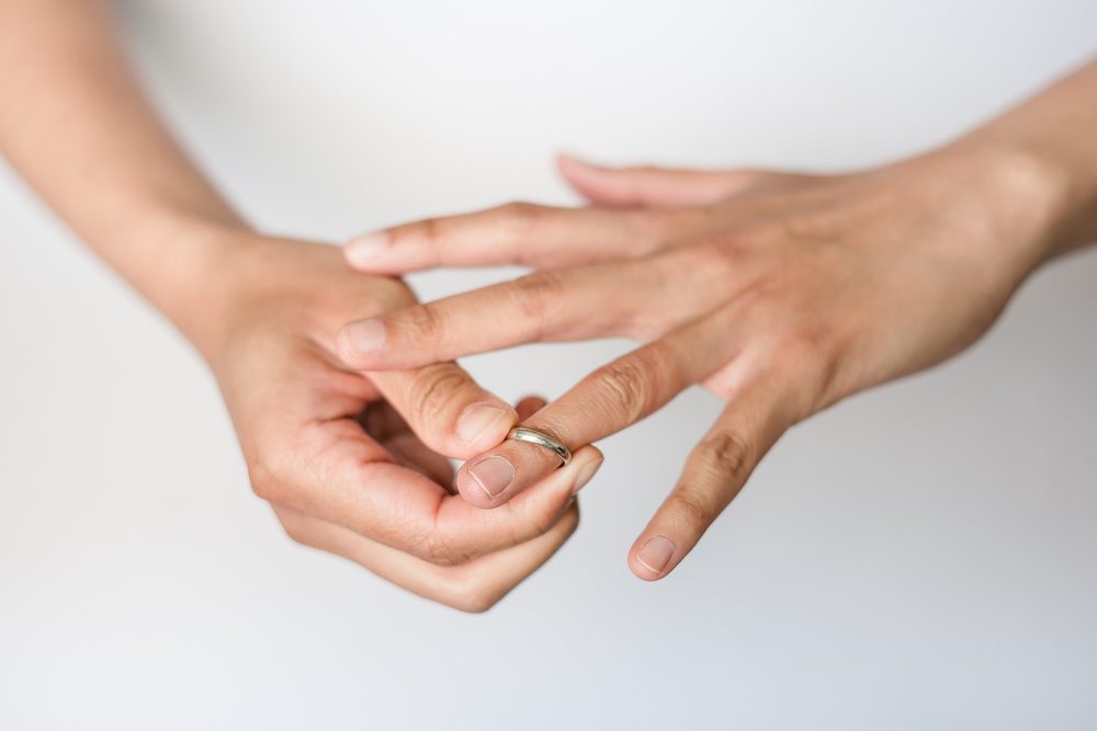 A woman is taking off her wedding ring from her finger.