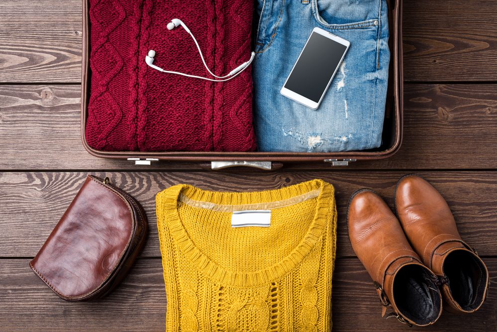 Open suitcase with casual female winter clothes on wooden table. Top view