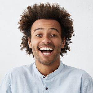 Carefree joyful handsome Afro American man with bushy hairstyle and bristle having shining eyes opening his mouth with joy bursting into laughing. Positive human expressions, emotions and feelings