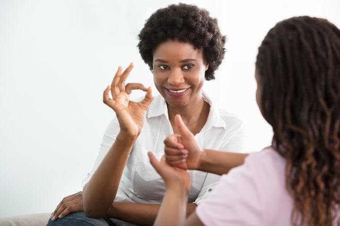 Smiling Young Mother Learning Sign Language To Talk With Her Hearing Impairment Daughter