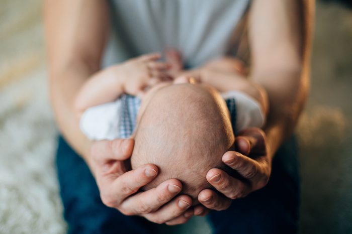 Father holding head of his newborn son in hands. Loving father hand holding cute sleeping newborn baby child