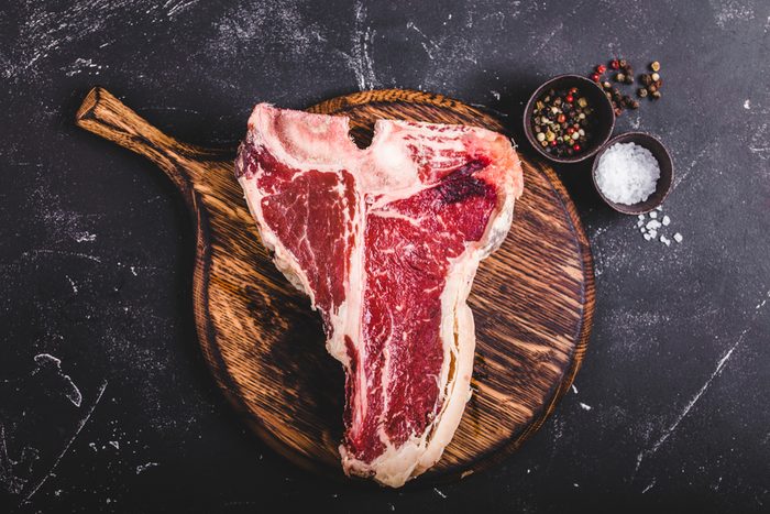Raw marbled meat steak T-bone, seasoning, wooden cutting board, rustic stone background. Beef T-bone steak, ready for cooking. Top view. Ingredients for meat roasting. T-bone steak. Meat steak concept